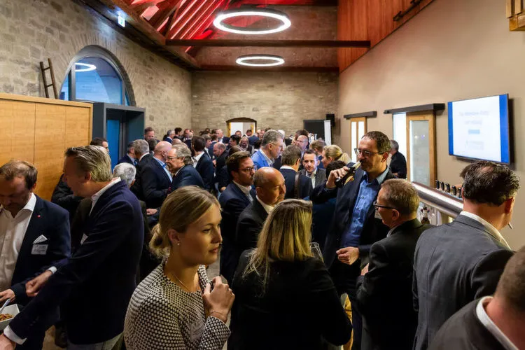 Eine Gruppe von Menschen in Businesskleidung versammelt sich in einem Raum für ein Networking-Event.