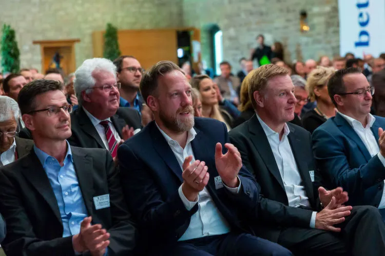 Eine Gruppe von Menschen in formeller Kleidung sitzt in einem Publikum und applaudiert.