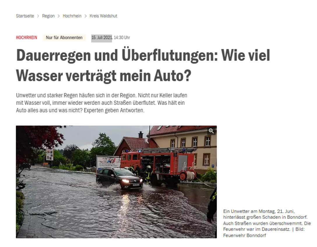 Ein Auto fährt durch eine überflutete Straße neben einem Feuerwehrfahrzeug.