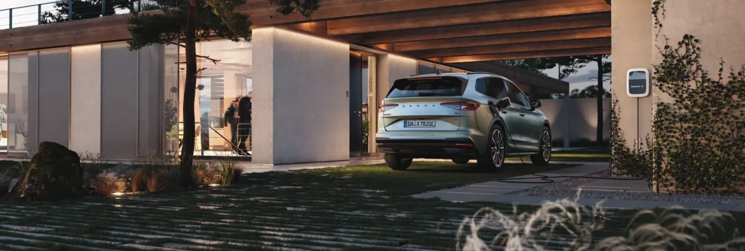 Ein Skoda Enyaq iV ist an einer Ladestation vor einem modernen Haus geparkt.