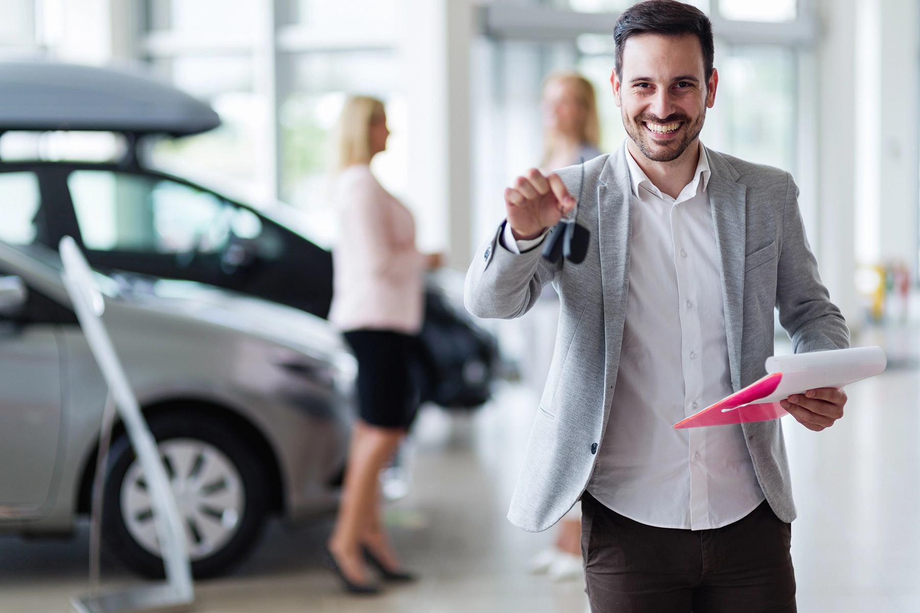 Autohaus-Waser-der-Kunde-im-Mittellpunkt Ein lächelnder Mann in einem Autohaus hält Autoschlüssel in der Hand.