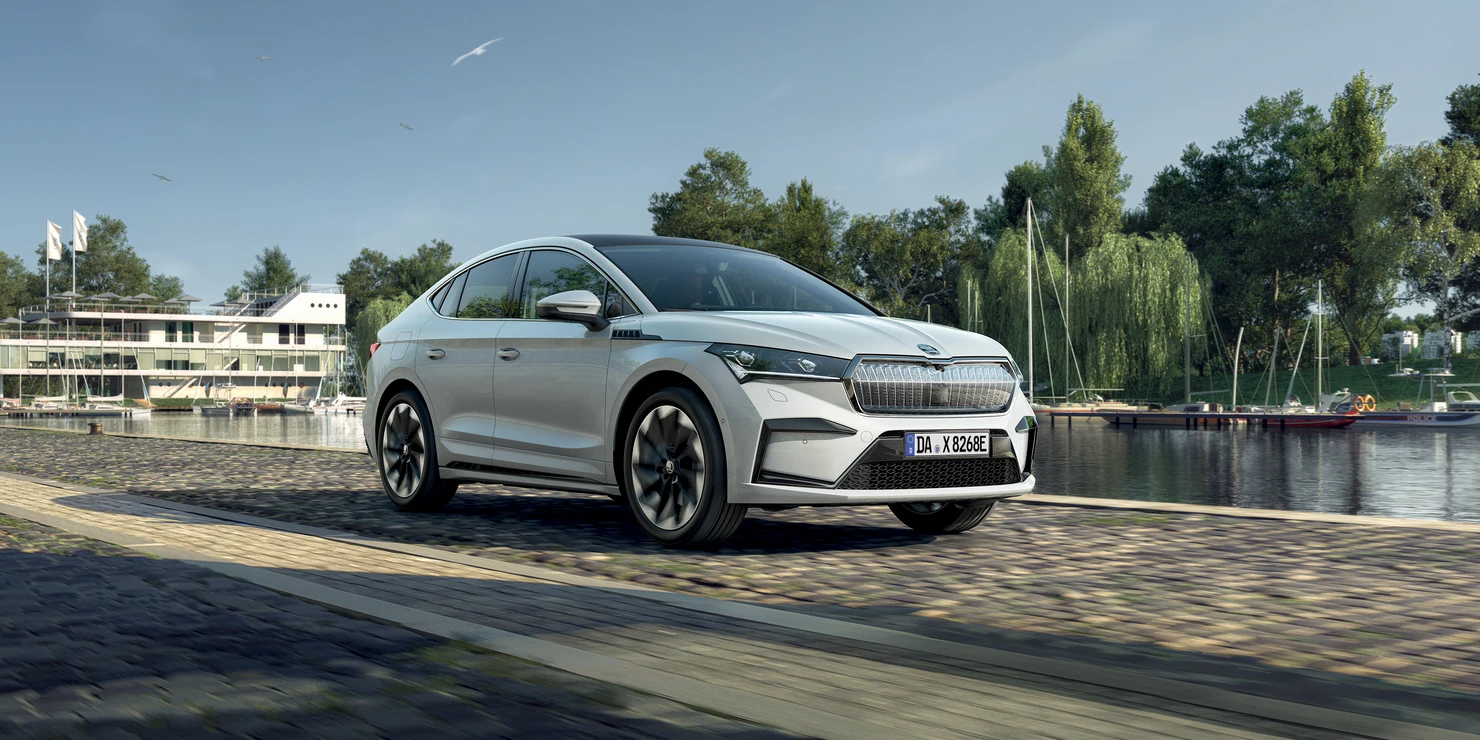 enyaq-coupe_2024_001 Ein weißer Škoda Enyaq Coupé 2024 fährt an einem Fluss entlang.