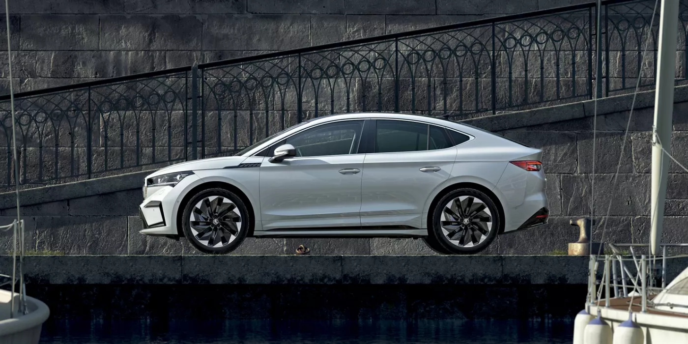 Ein weißes Škoda Enyaq Coupé 2024 steht seitlich vor einer Steinmauer.