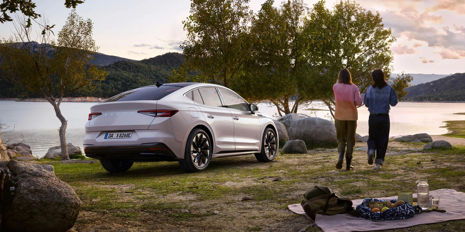Ein Skoda Enyaq Coupé 2024 steht an einem Seeufer, während zwei Personen spazieren gehen.