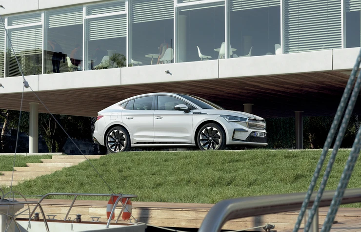 enyaq-coupe_2024_004 Ein weißer Škoda Enyaq Coupé 2024 parkt vor einem modernen Gebäude.