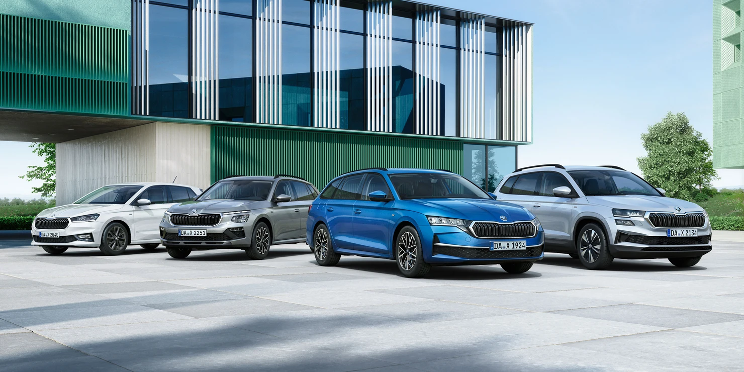 header-explore-and-more Vier Skoda-Autos verschiedener Modelle stehen nebeneinander vor einem modernen Gebäude.