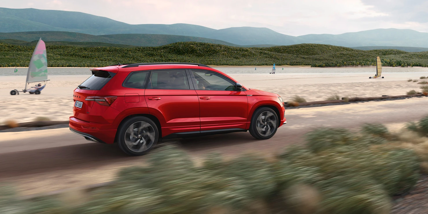 Ein roter Škoda Karoq Sportline fährt auf einer Küstenstraße.