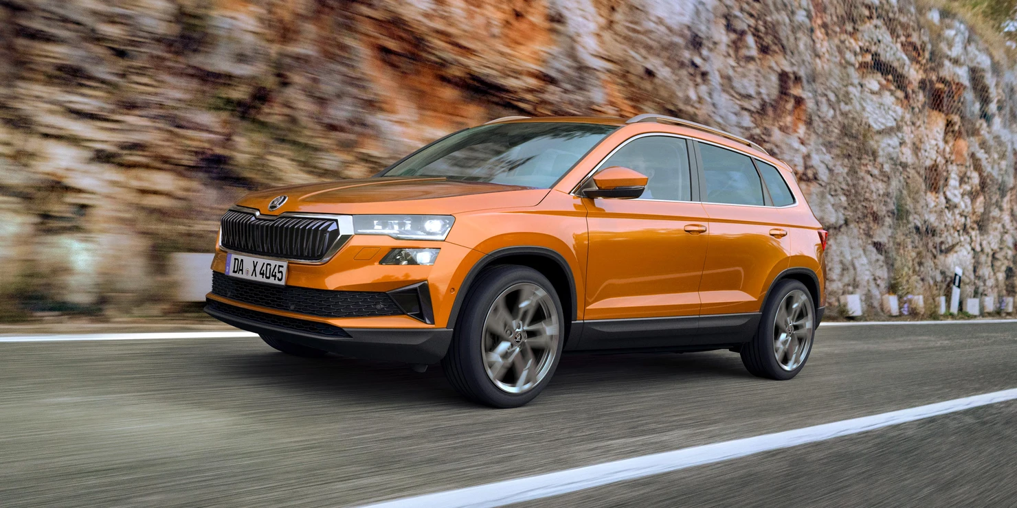Ein orangefarbener Škoda Karoq fährt auf einer Straße entlang einer Felswand.