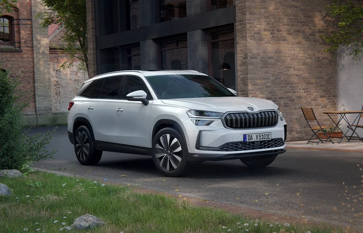 Ein weißer Škoda Kodiaq iV steht auf einer Straße vor einem Gebäude.