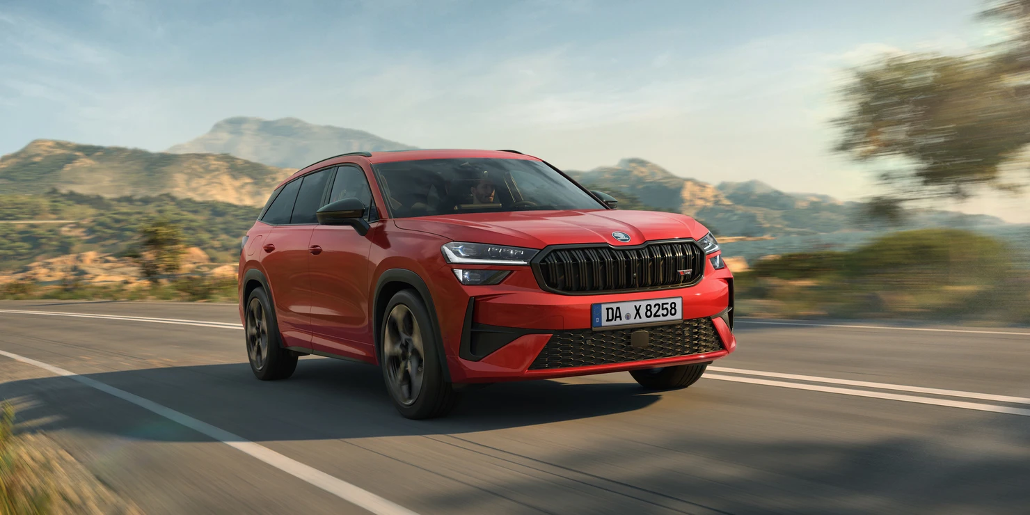 Ein roter Škoda Kodiaq RS fährt auf einer Landstraße vor einer bergigen Landschaft.