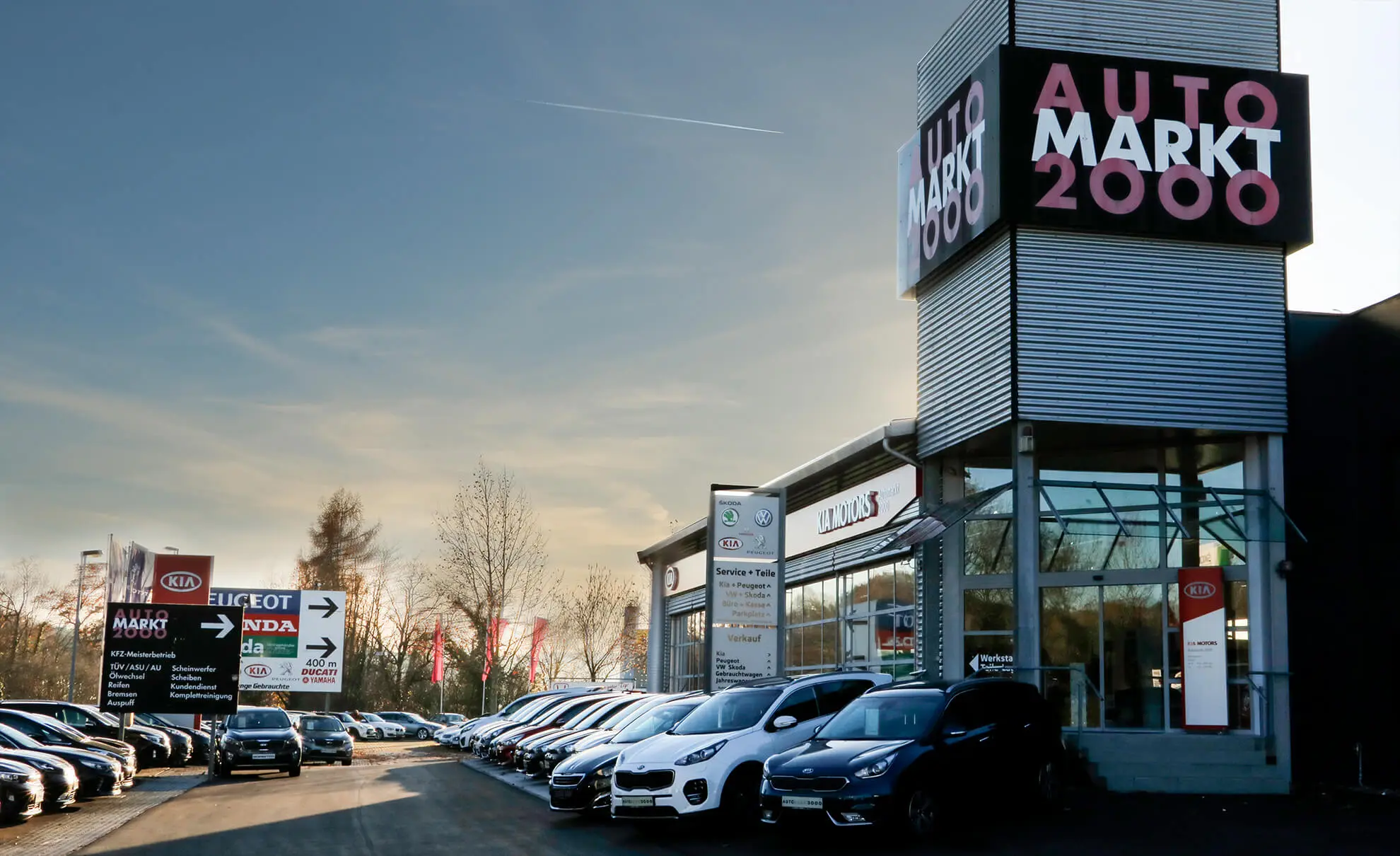Autmarkt2000-Gelände Autohaus mit mehreren geparkten Autos und einem Schild mit der Aufschrift "AutoMarkt 2000".