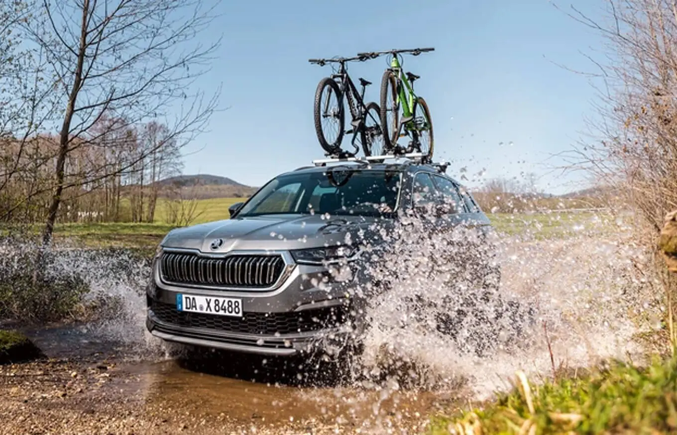 garantieverlängerung_bp1920_1 Ein Škoda SUV fährt durch eine Wasserpfütze mit zwei Fahrrädern auf dem Dach.