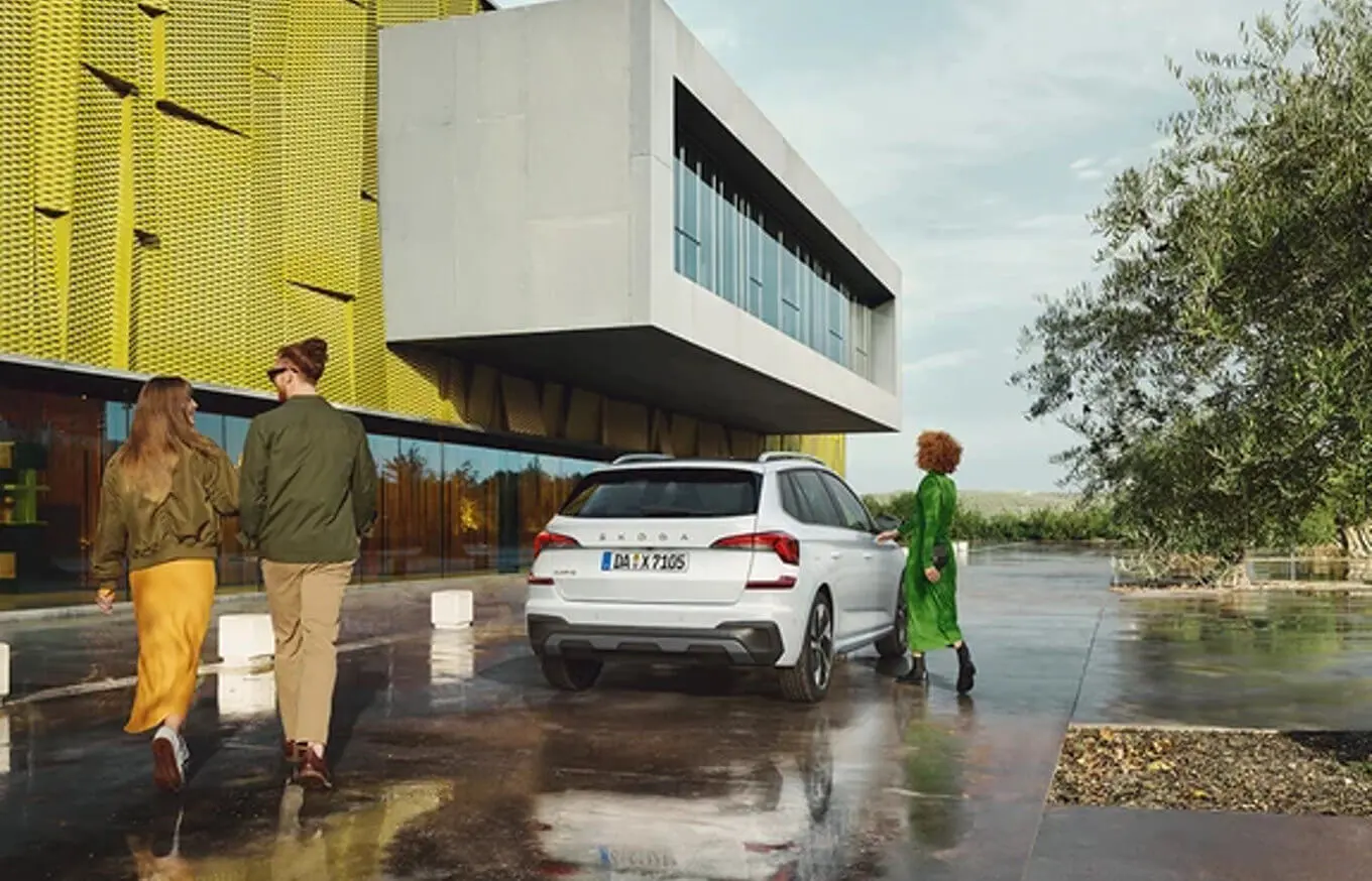 herstellergarantie_bp320_1 Drei Personen stehen neben einem weißen Škoda-Auto vor einem modernen Gebäude.