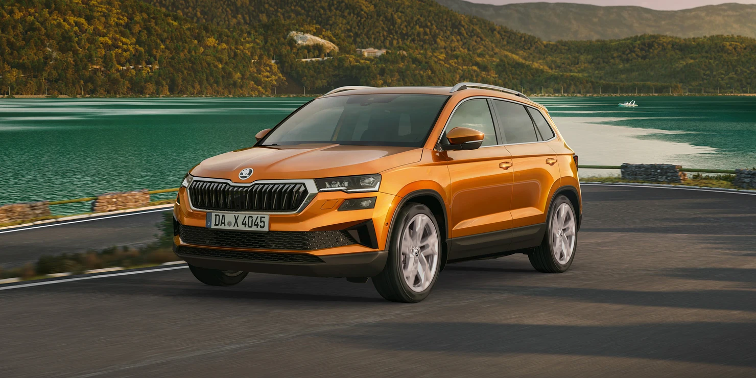 Ein orangefarbener Škoda Karoq 2025 fährt auf einer Straße entlang eines Sees.