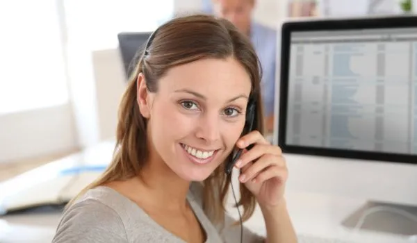 kontakt Eine lächelnde Frau mit Headset sitzt vor einem Computerbildschirm.