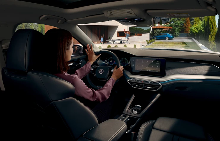 octavia-slider_03 Eine Frau sitzt am Steuer eines Skoda Octavia und blickt nach draußen auf ein modernes Haus.