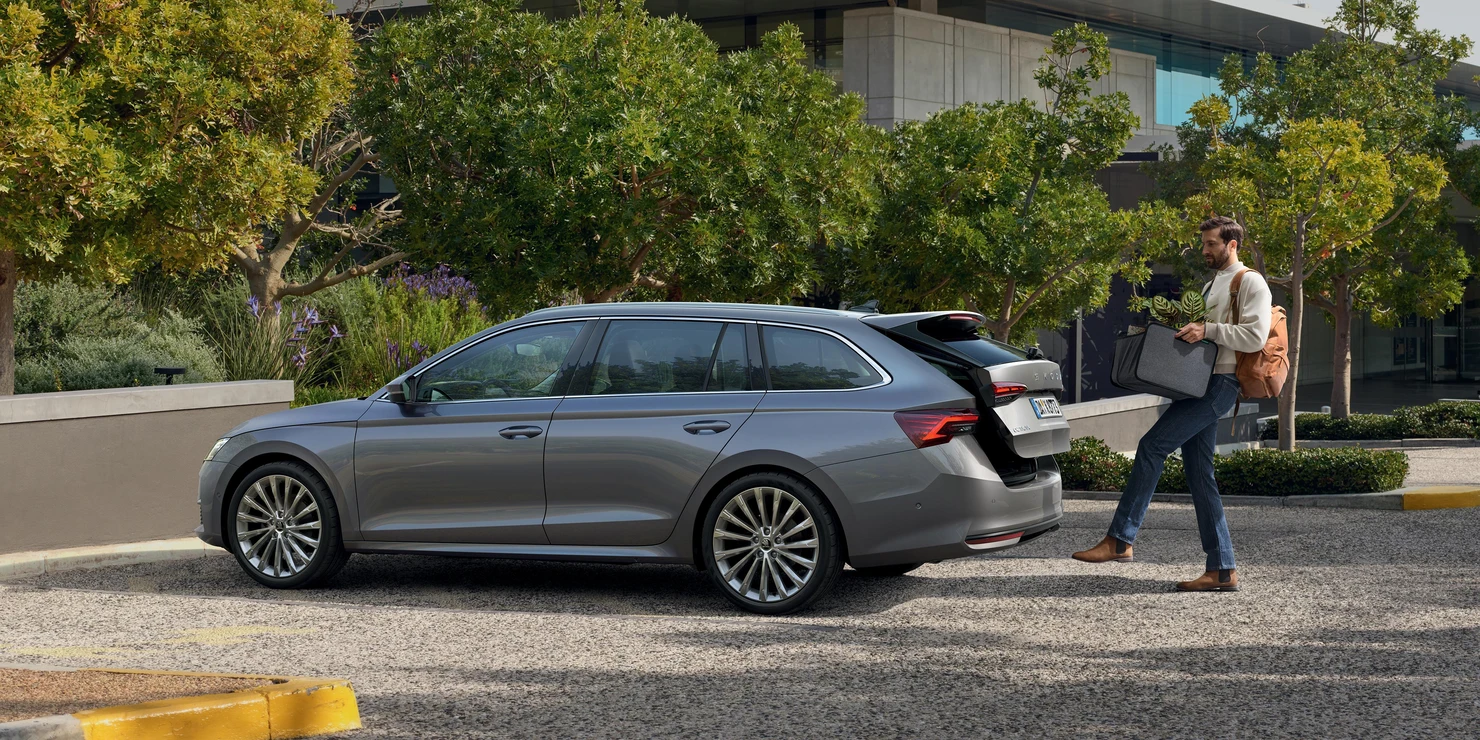 Ein Mann steht vor einem grauen Skoda Octavia Combi 2025 und öffnet den Kofferraum mit dem Fuß.