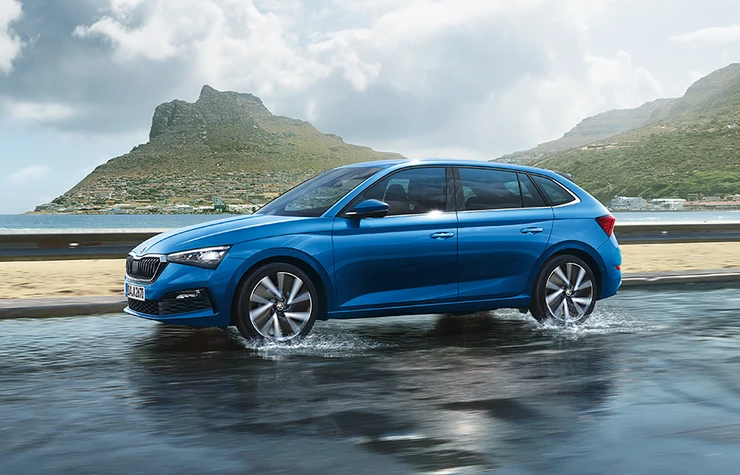 Ein blauer Skoda Scala fährt auf einer nassen Straße vor einer bergigen Küstenlandschaft.