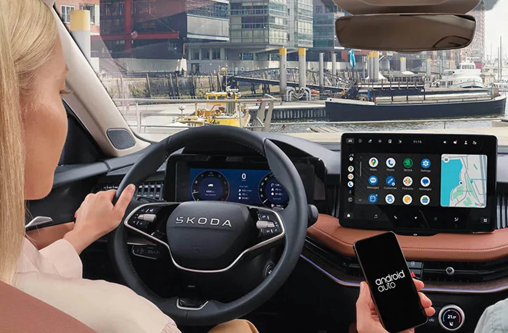Frau fährt einen Škoda mit Android Auto auf dem Display und hält ein Smartphone.