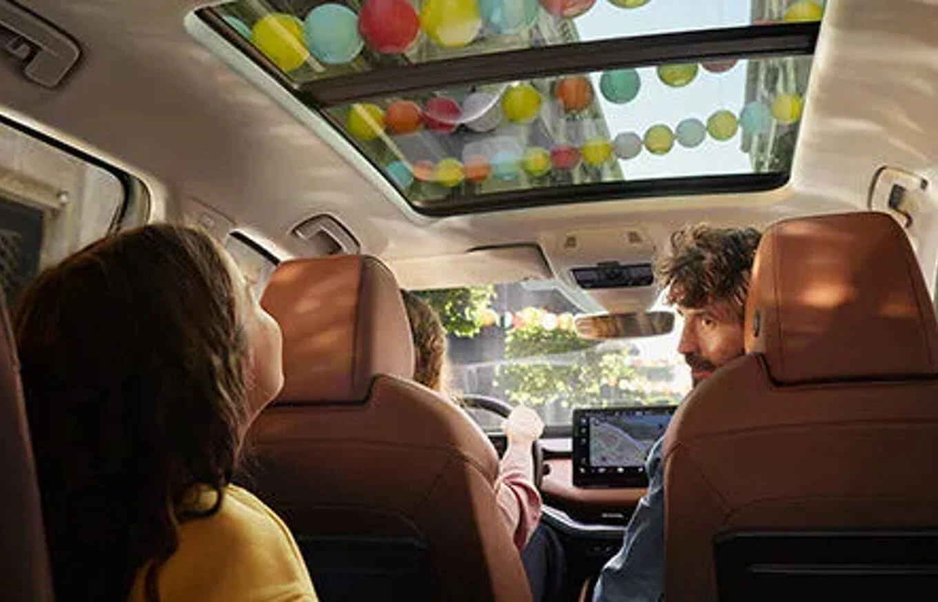 skoda-connect-infotainment Personen im Auto schauen durch ein Panoramadach mit bunten Luftballons darüber.