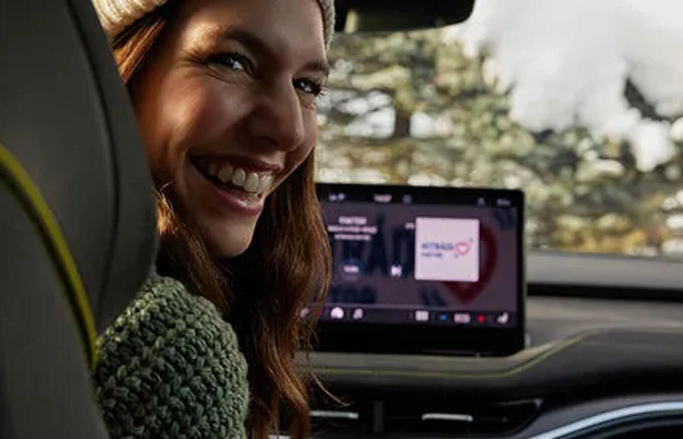 smart-link+ Eine lächelnde Person sitzt in einem Auto mit einem Bildschirm im Hintergrund.