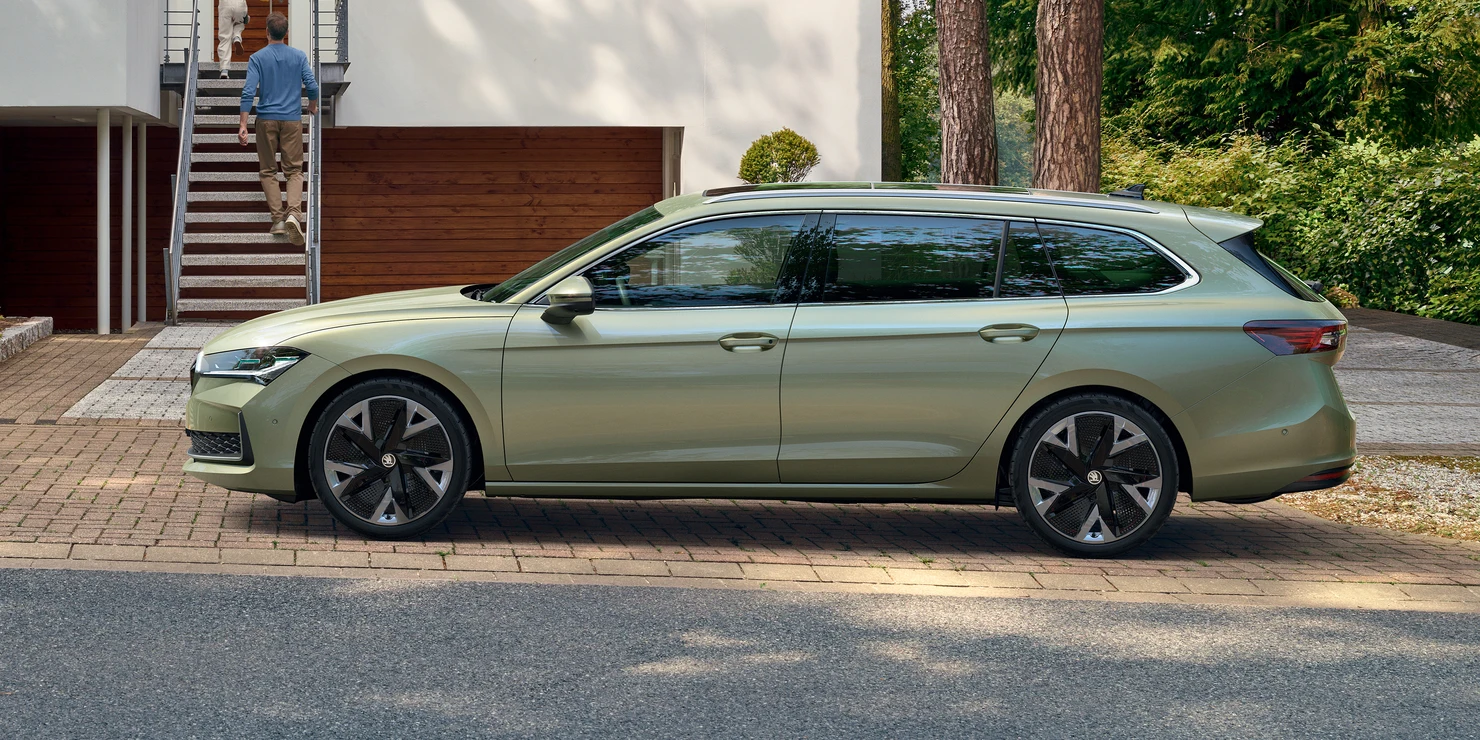 Ein grüner Škoda Superb Combi steht auf einer Straße vor einem modernen Gebäude.