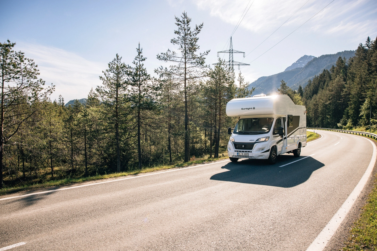 Camper-Mieten Wohnmobil Sunlight A60 fährt auf einer Landstraße durch eine Waldlandschaft.