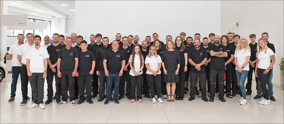 Gruppe von Menschen in Arbeitskleidung posiert für ein Gruppenfoto in einem Autohaus.