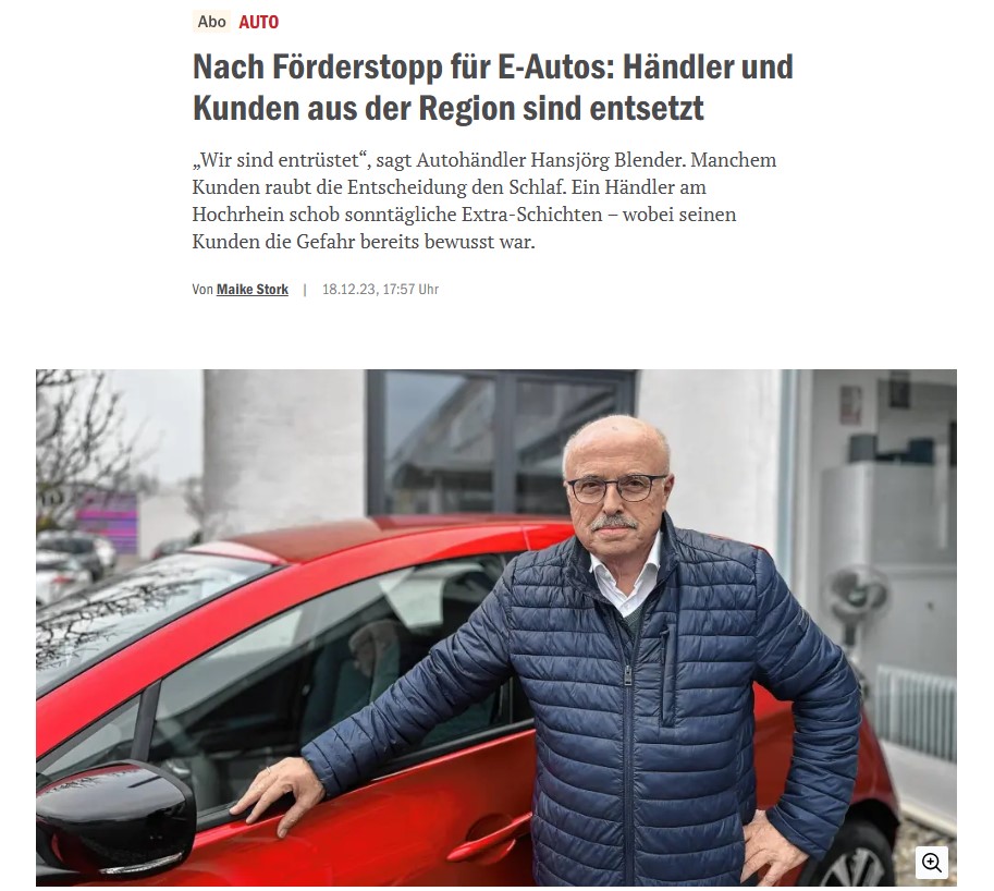 Ein Mann steht neben einem roten Auto vor einem Gebäude.