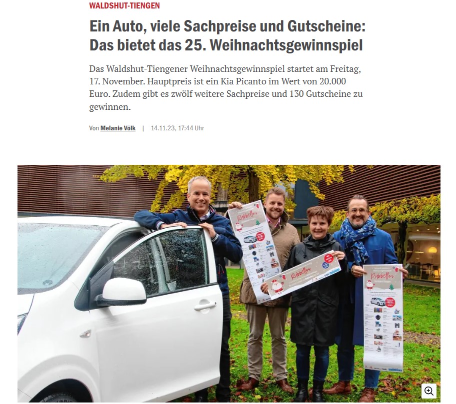 Vier Personen stehen lächelnd mit Plakat neben einem weißen Kia Picanto.