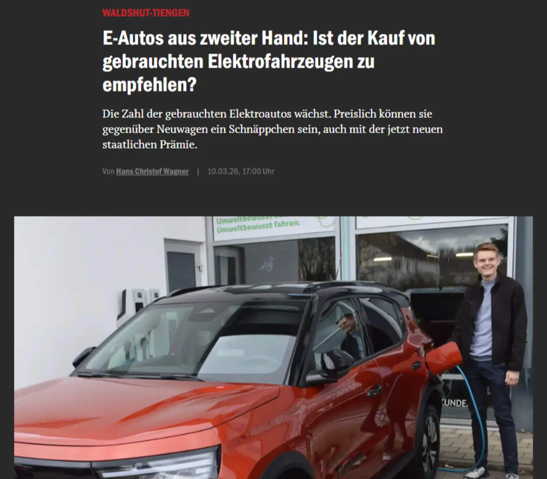 Ein Mann lädt ein rotes Elektroauto an einer Ladestation auf.