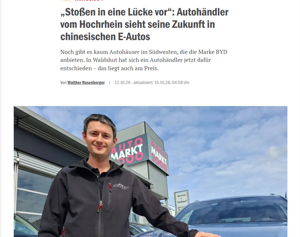 Ein Mann steht neben einem Auto vor einem Autohaus.